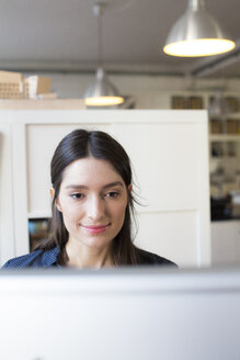 Lächelnde Frau schaut auf den Computerbildschirm am Schreibtisch im Büro - FKF02299