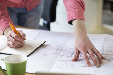 Close-up of man working on blueprint at desk in office - FKF02306