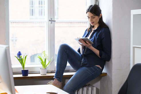 Woman using tablet at the window in office - FKF02313