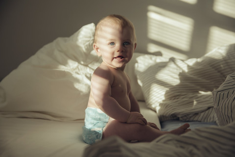 Baby boy sitting in bed in shadow and sunlight stock photo