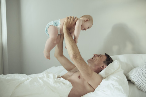 Happy mature father lifting up his baby son in bed stock photo