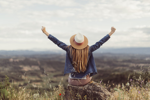 Rückenansicht einer rothaarigen Frau, die auf einem Felsen sitzt und in die Ferne schaut, lizenzfreies Stockfoto