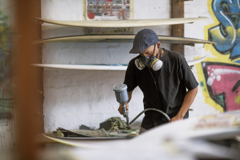 Werkstatt für Surfboard-Shaper, Mitarbeiter eines Surfboard-Shops beim Besprühen eines Surfboards, lizenzfreies Stockfoto