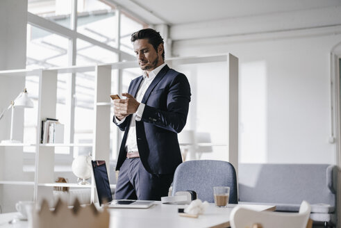 Businessman using cell phone in office - KNSF01284