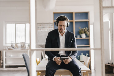 Businessman with tablet and headphones sitting on table - KNSF01287