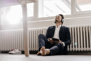 Businessman with tablet and headphones sitting on floor - KNSF01289