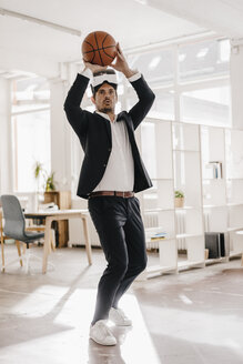 Businessman wearing VR glasses playing basketball in office - KNSF01292