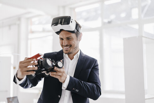 Smiling businessman wearing VR glasses looking at toy racing car - KNSF01335