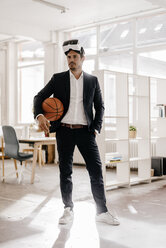 Businessman wearing VR glasses holding basketball in office - KNSF01336