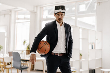 Businessman wearing VR glasses holding basketball in office - KNSF01337