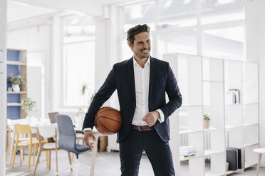 Businessman holding basketball in office - KNSF01338