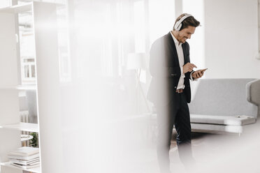 Smiling businessman with cell phone and headphones - KNSF01340