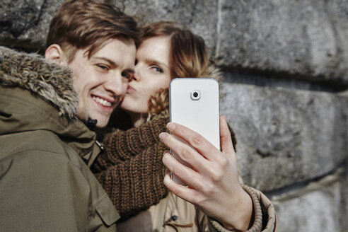 Glückliches junges Paar, das sich im Freien küsst und ein Selfie macht - ANHF00034