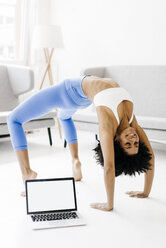 Young woman practising yoga with laptop by her side - KNSF01378