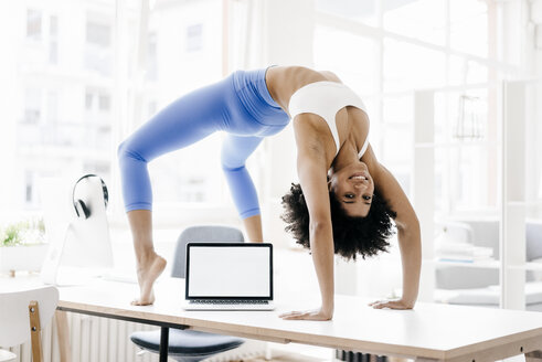 Young woman practising yoga with laptop by her side - KNSF01380