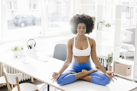 Junge Frau übt Yoga auf ihrem Schreibtisch, lizenzfreies Stockfoto