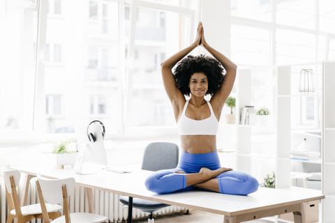 Junge Frau übt Yoga auf ihrem Schreibtisch, lizenzfreies Stockfoto