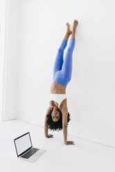 Young woman practising yoga with laptop by her side - KNSF01409