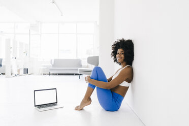 Fit young woman sitting on floor with laptop by her side - KNSF01410