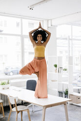 Young woman doing yoga on her desk - KNSF01420