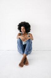 Young woman sitting on floor, laughing - KNSF01423