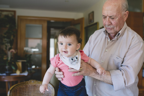 Happy Baby girl standing with help of Great-grandfather at home stock photo