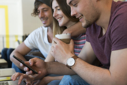 Three friends using cell phone and laptop in a cafe - KKAF00813