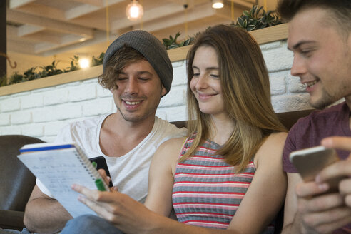 Three friends with notepad and cell phones in a cafe - KKAF00820