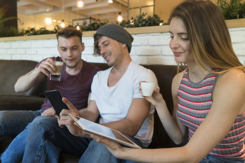 Drei Freunde benutzen Tablet und Mobiltelefon in einem Café, lizenzfreies Stockfoto