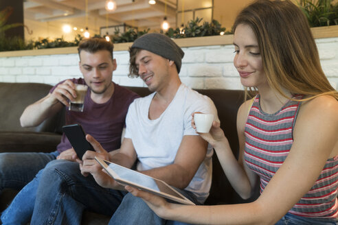Drei Freunde benutzen Tablet und Mobiltelefon in einem Café - KKAF00821