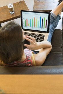 Young woman using cell phone and laptop with bar chart in a cafe - KKAF00828