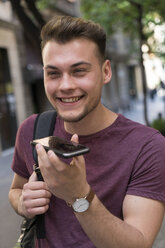 Glücklicher junger Mann, der in der Stadt ein Mobiltelefon benutzt - KKAF00848
