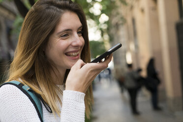 Glückliche junge Frau, die in der Stadt ein Mobiltelefon benutzt - KKAF00849