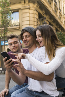 Drei Freunde benutzen ein gemeinsames Handy in der Stadt - KKAF00854