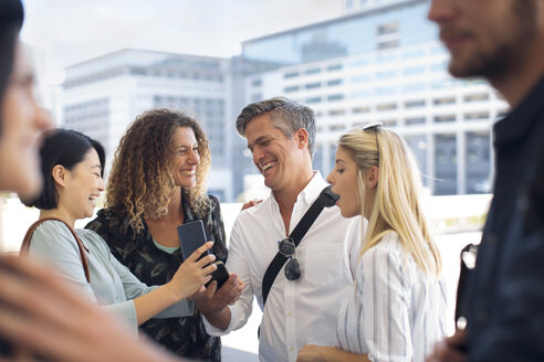 Gruppe von glücklichen Geschäftsleuten, die sich auf einem städtischen Platz ein Handy teilen - ZEF13707