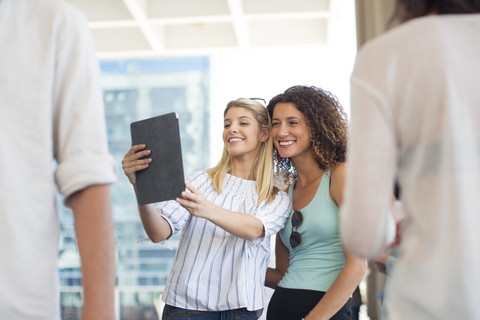 Two happy women taking a selfie with tablet on urban square stock photo