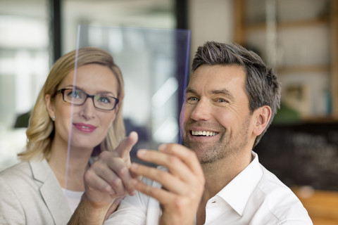 Ein lächelnder Geschäftsmann und eine Frau benutzen ein futuristisches tragbares Gerät, lizenzfreies Stockfoto
