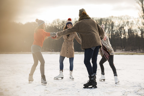 Friends ice skating in a circle on frozen lake stock photo