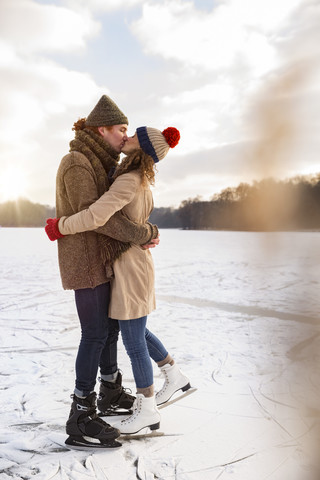 Couple with ice skates kissing on frozen lake stock photo