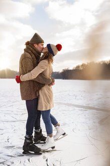 Paar mit Schlittschuhen, das sich auf einem zugefrorenen See küsst - MFF03540