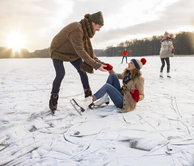 Man helping ice skating woman up on icy surface of frozen lake - MFF03541
