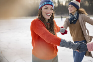 Female friends ice skating in a circle on frozen lake - MFF03542