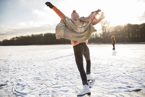 Rückansicht einer Frau mit Schlittschuhen auf einem zugefrorenen See, lizenzfreies Stockfoto