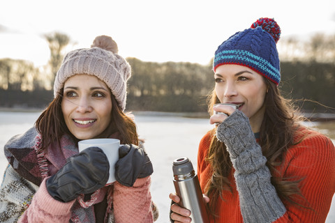 Two women drinking hot beverages outdoors in winter stock photo