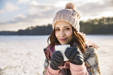 Portrait of smiling woman drinking hot beverage from a cup outdoors in winter - MFF03560