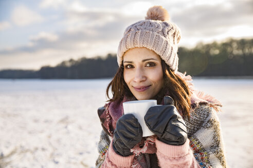 Porträt einer lächelnden Frau, die ein heißes Getränk aus einer Tasse im Freien im Winter trinkt - MFF03560