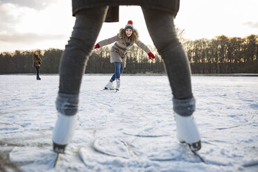 Woman ice skating on frozen lake with friends - MFF03567