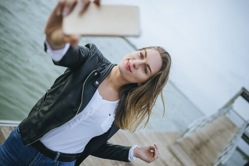 Porträt einer lächelnden jungen Frau, die ein Selfie an der Strandpromenade macht - KIJF01503