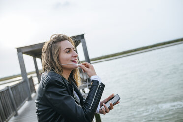 Young woman on the phone standing on boardwalk - KIJF01506