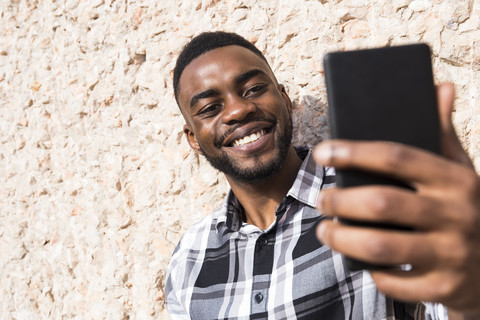 Porträt eines lächelnden jungen Mannes, der ein Selfie mit einem Mobiltelefon macht, lizenzfreies Stockfoto
